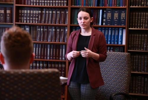 a student speaks to a professor in front of a wall of books