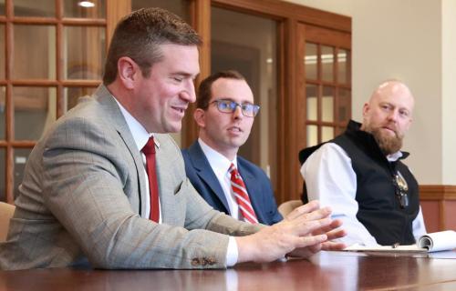 AGO Bailey speaks at a table with two other people onlooking